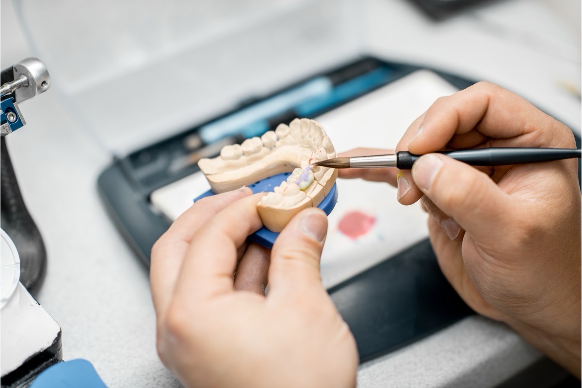 Hands painting fine detail onto a dental model at a laboratory bench