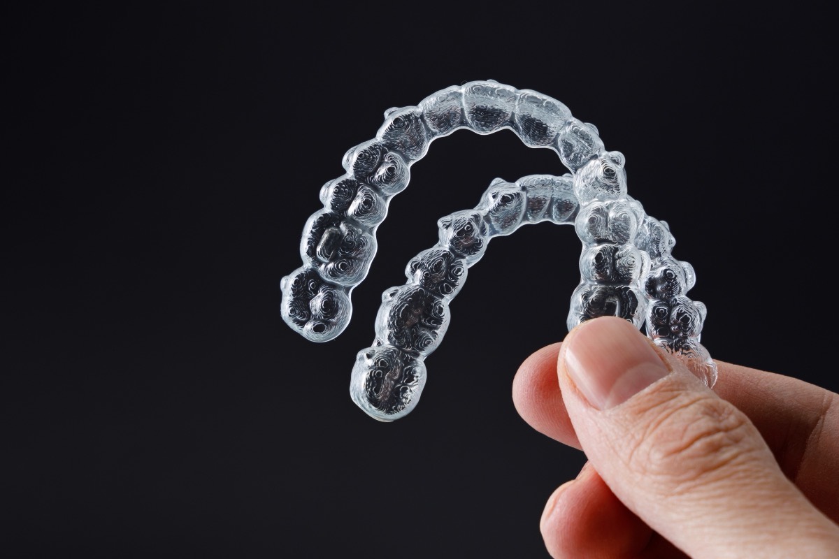 Hand holding a pair of clear aligners against a dark background